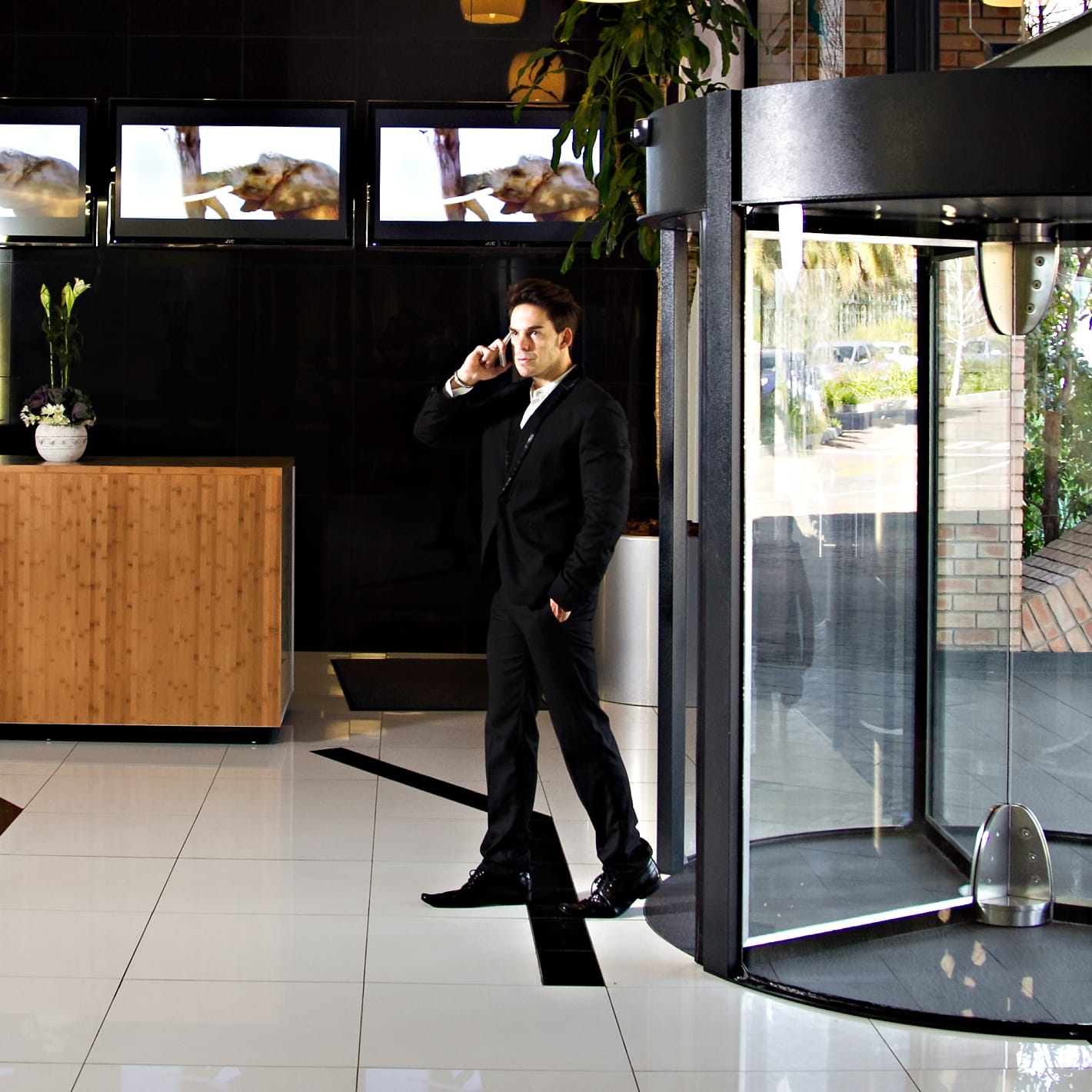 Man on the phone walking past a revolving door beside a hotel reception desk.