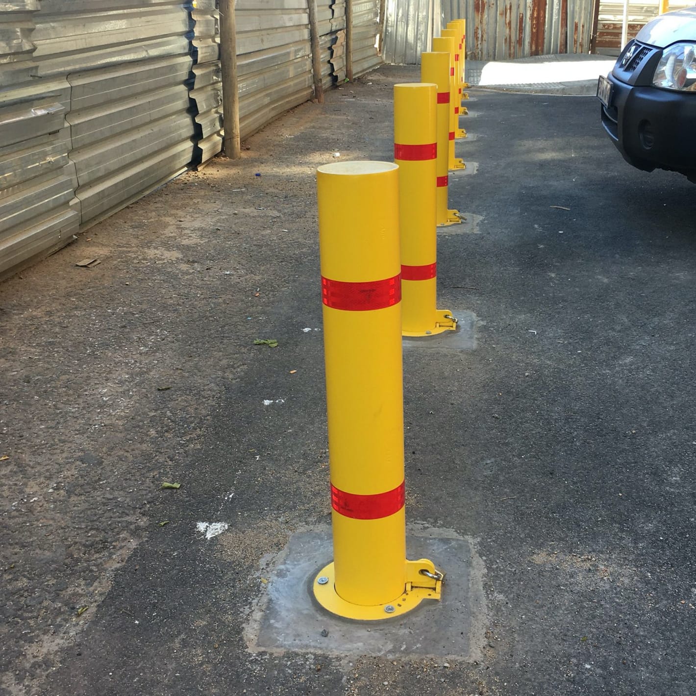 Line of yellow fixed bollards with red bands bolted down beside a site road.