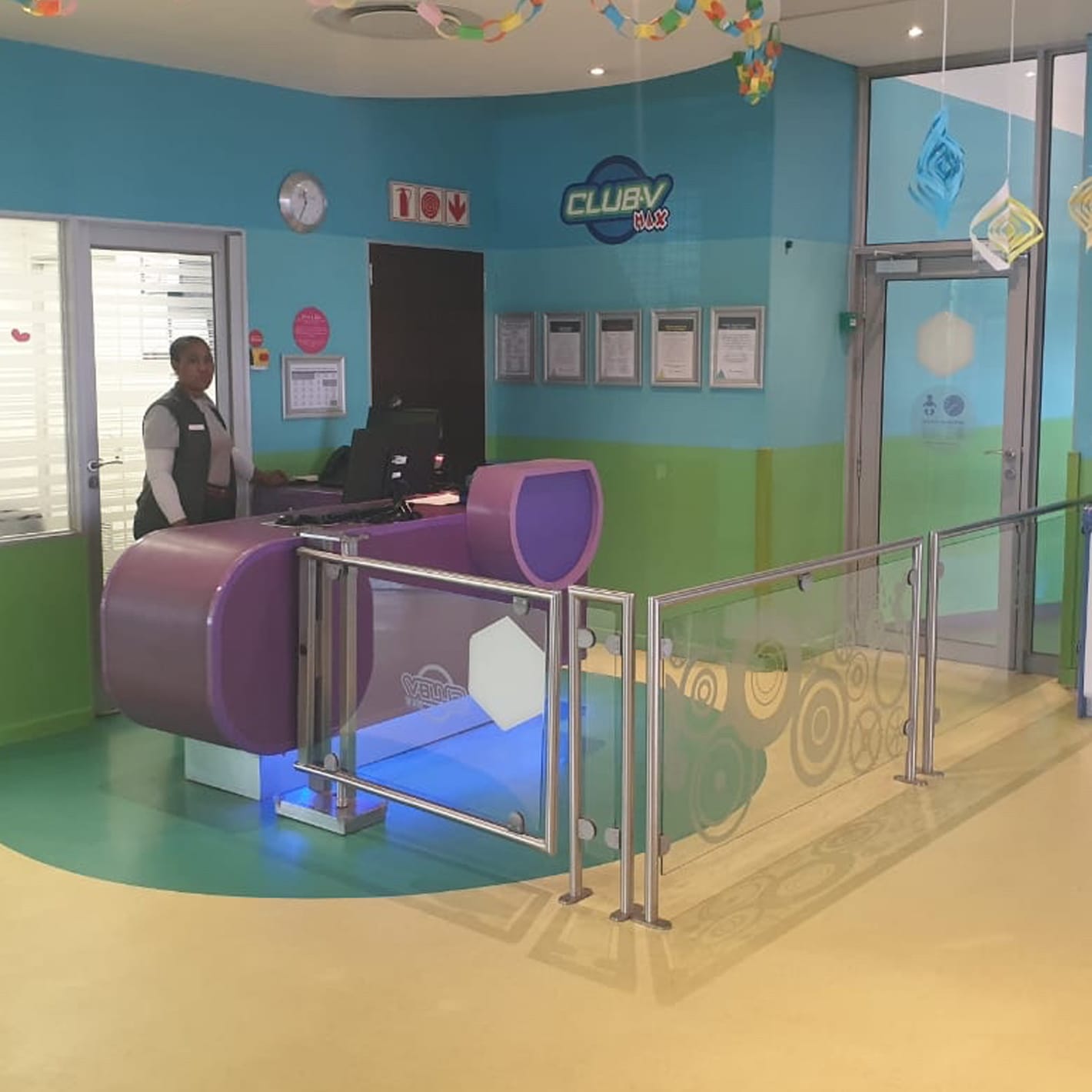 Stainless steel framed accessible gate installed at a reception desk beside a glass balustrade.