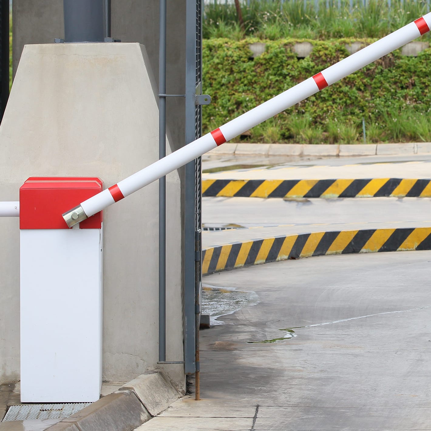 Traffic Master barrier with a red lid and raised boom beside a concrete wall at a ramp entrance.