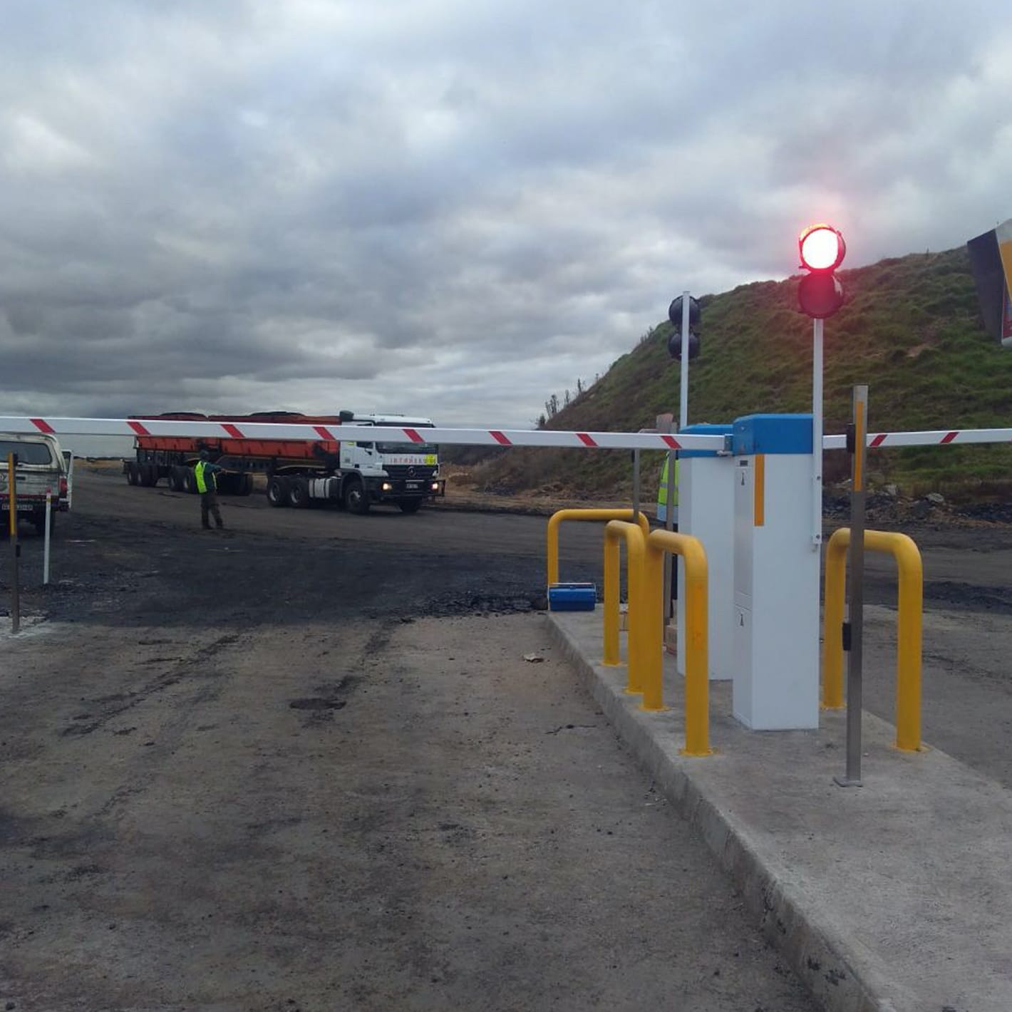 Traffic Master barriers and a traffic light at a truck entrance to an industrial yard, with yellow bollards.