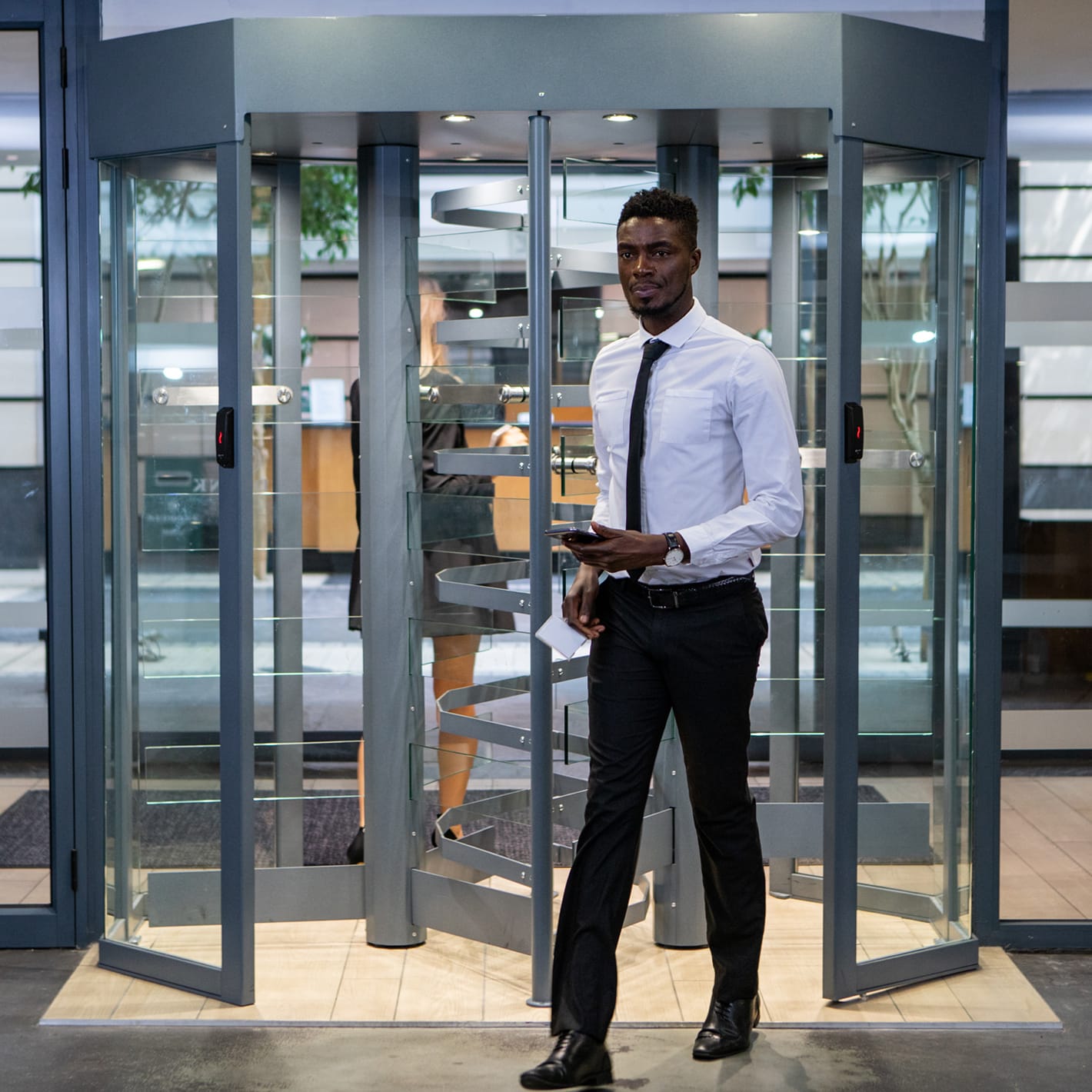 Man walking out of a double Triton octagonal glass turnstile in an office lobby.