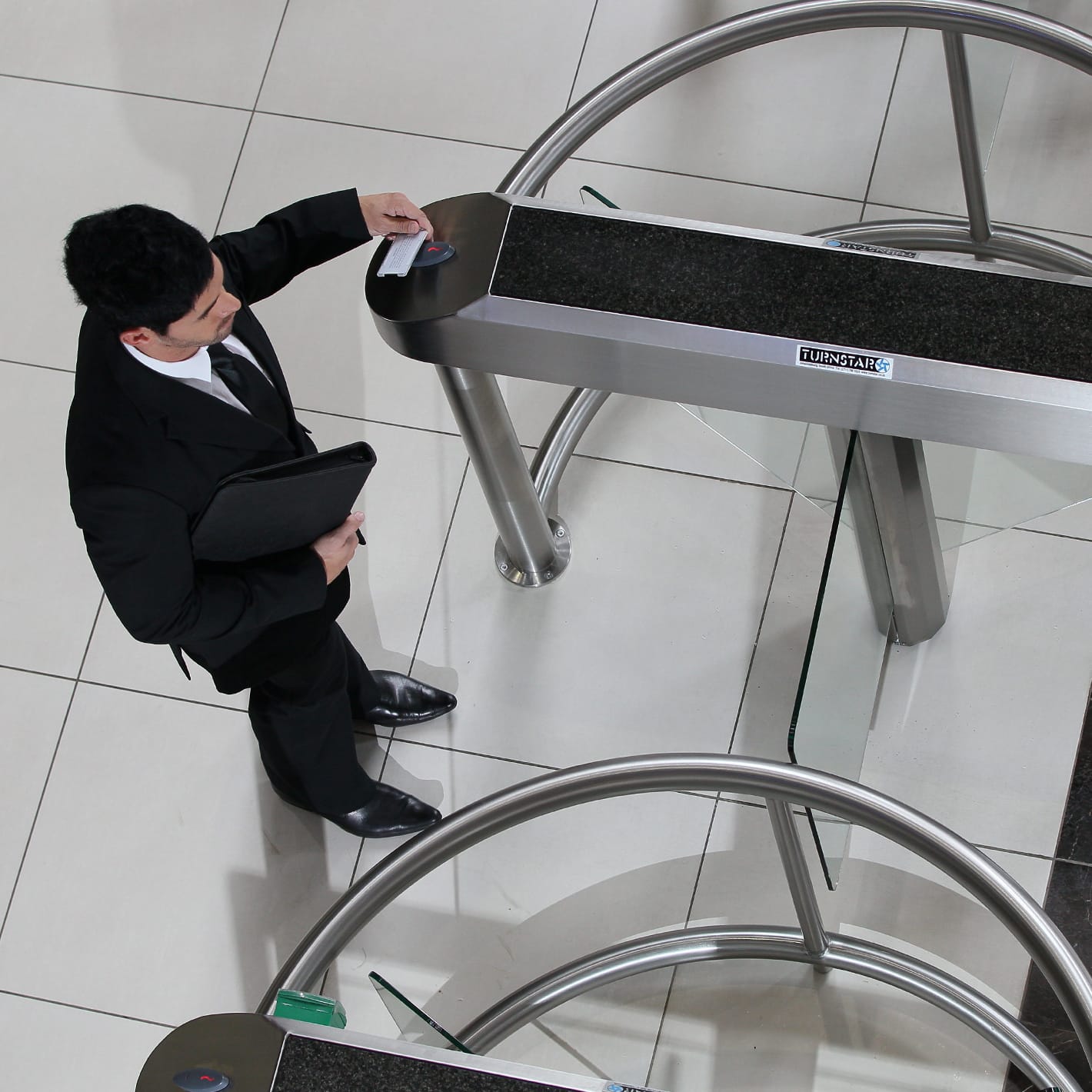 Man presenting a card at the reader of a Triton turnstile, seen from above.