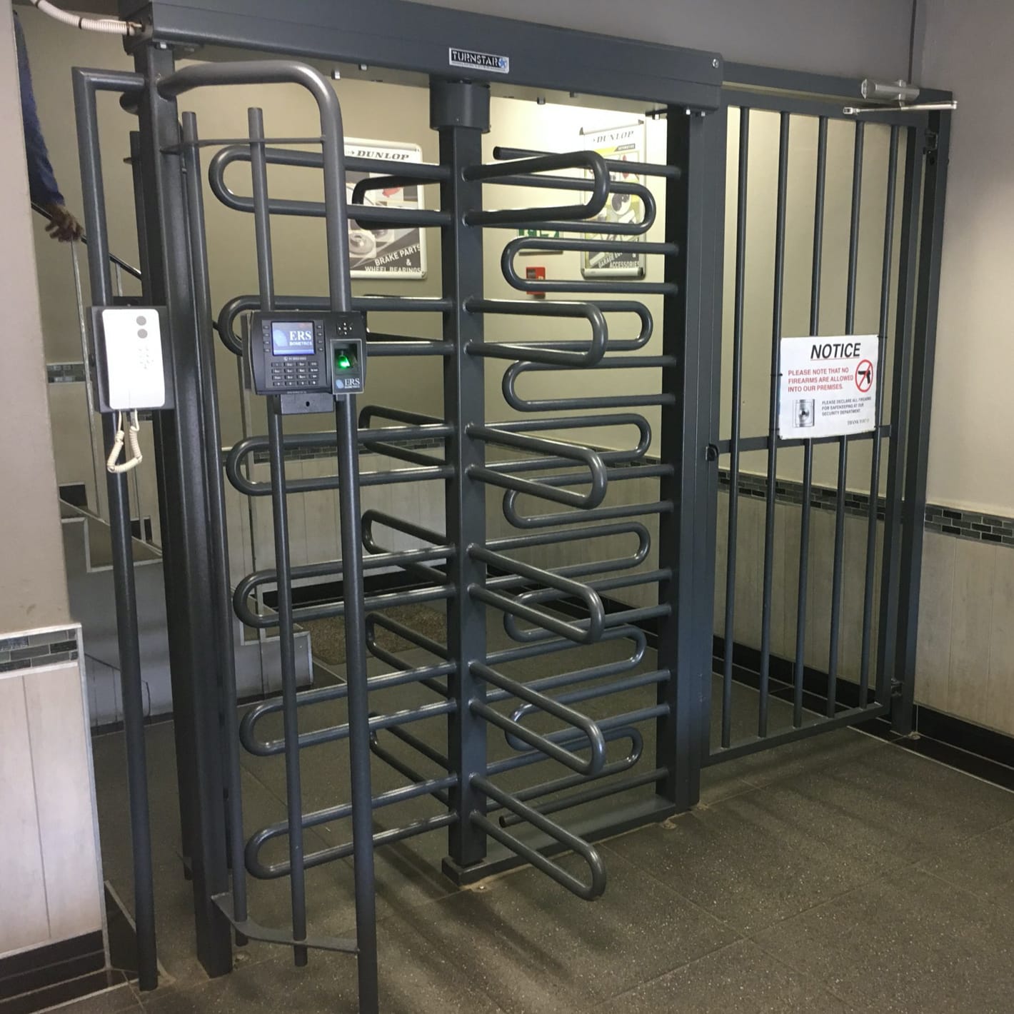 Grey Triumph full-height turnstile installed indoors with a fingerprint reader on the frame.