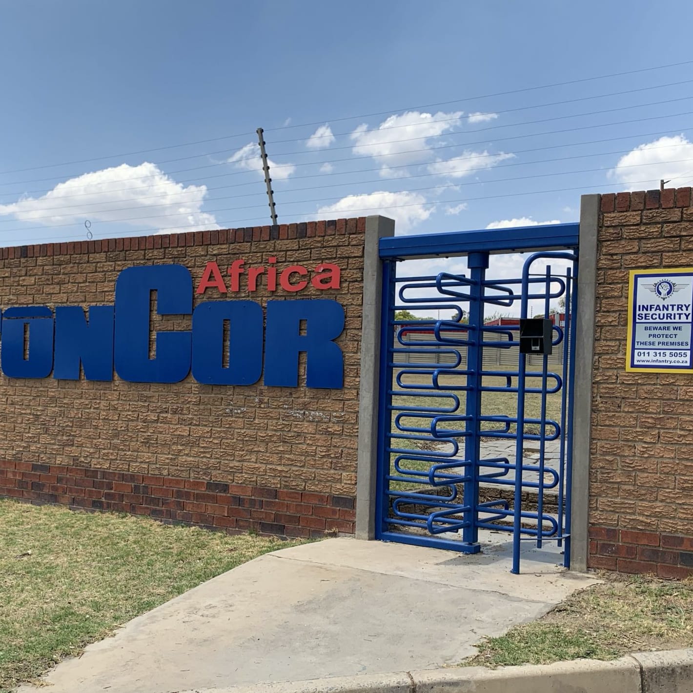 Blue Triumph full-height turnstile set into a brick wall at a company entrance.