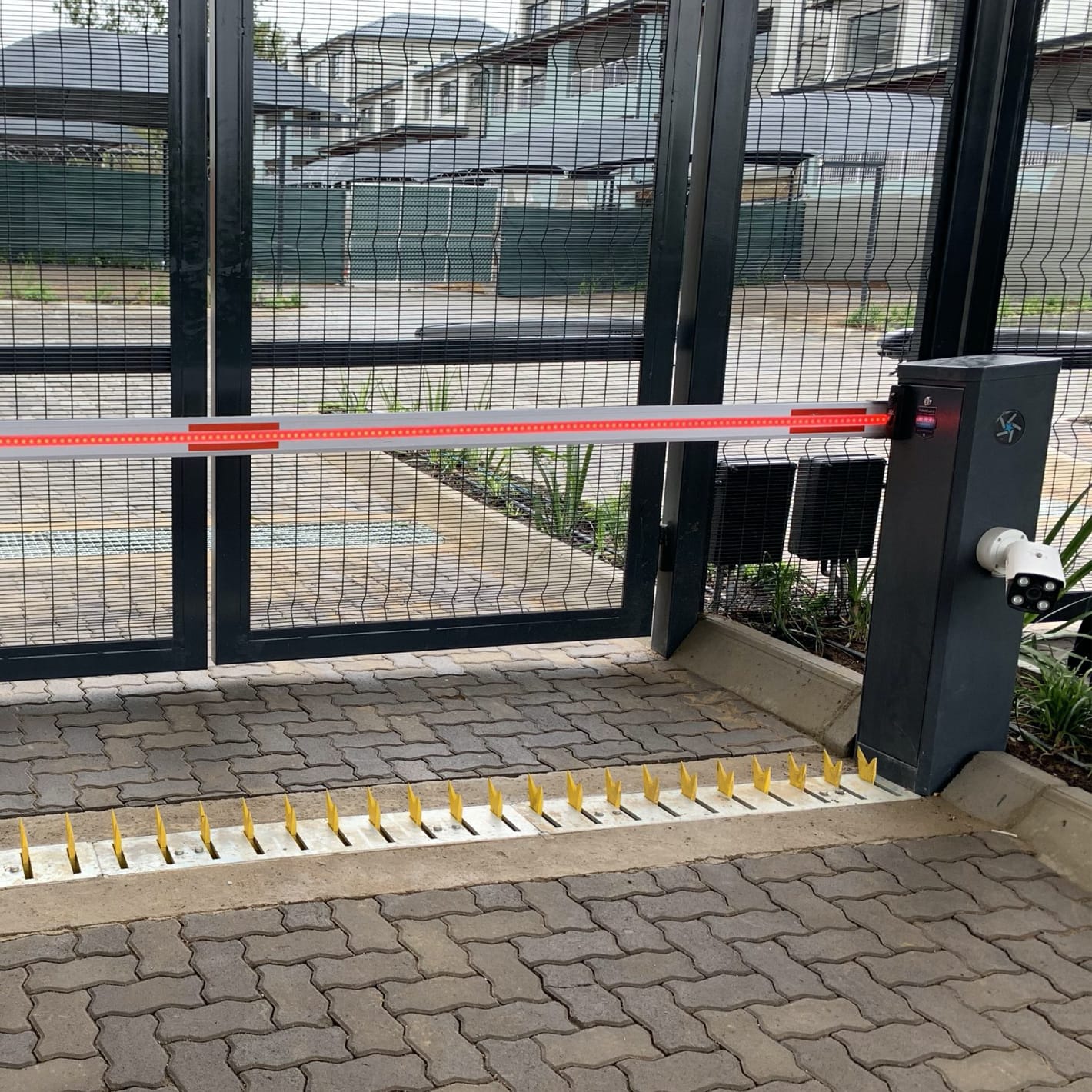 Velocity Raptor with a black cabinet and surface spike rack across a paved entrance in front of a gate.