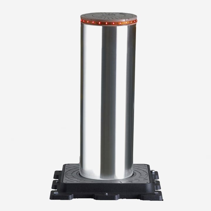 Automatic rising bollard with a metal post and red reflective band, standing on its ground casing.