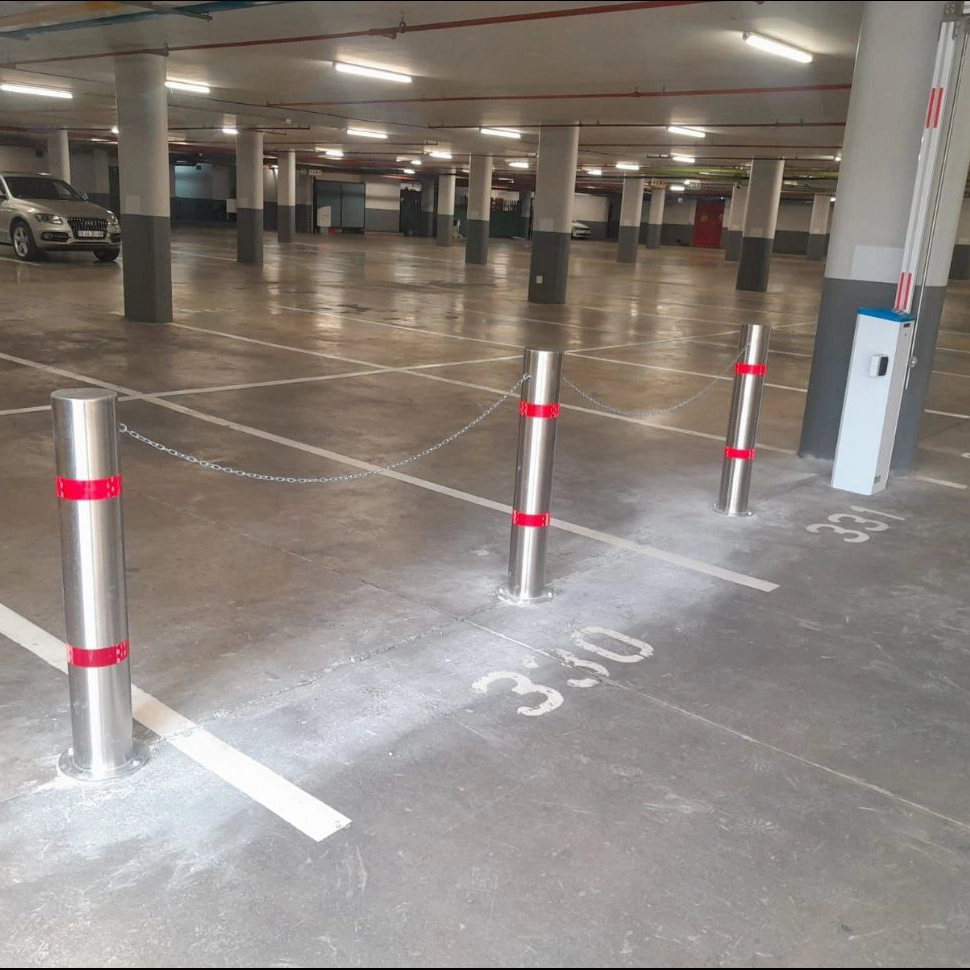 Metal fixed bollards with red bands protecting a walkway in an underground car park.