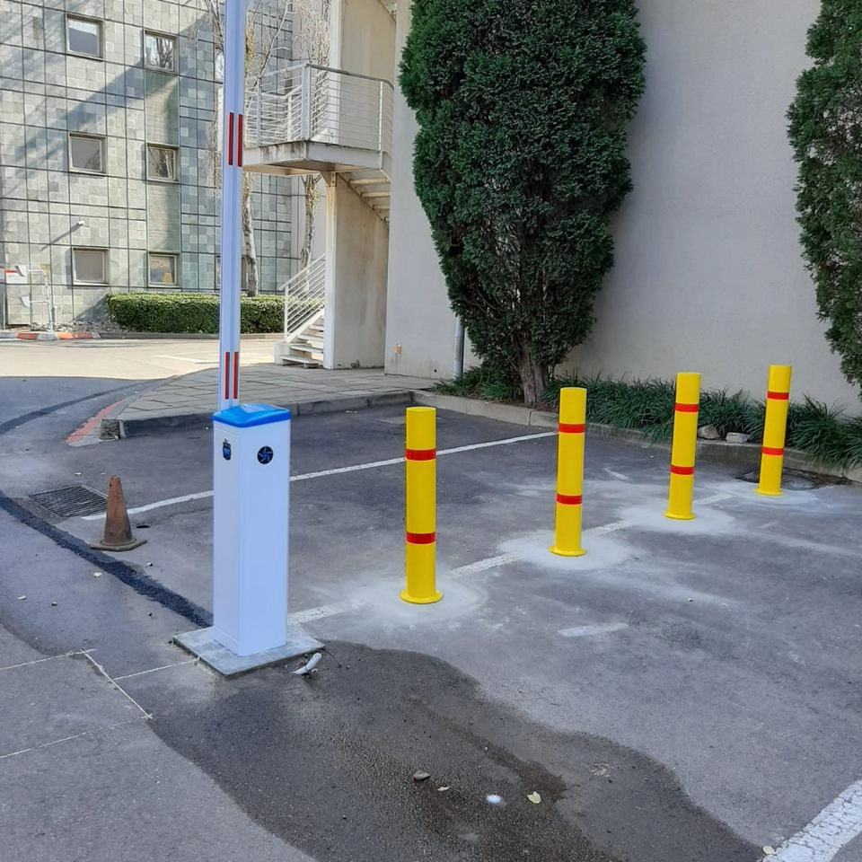 Yellow fixed bollards with red bands lining a parking area next to a boom barrier lane.