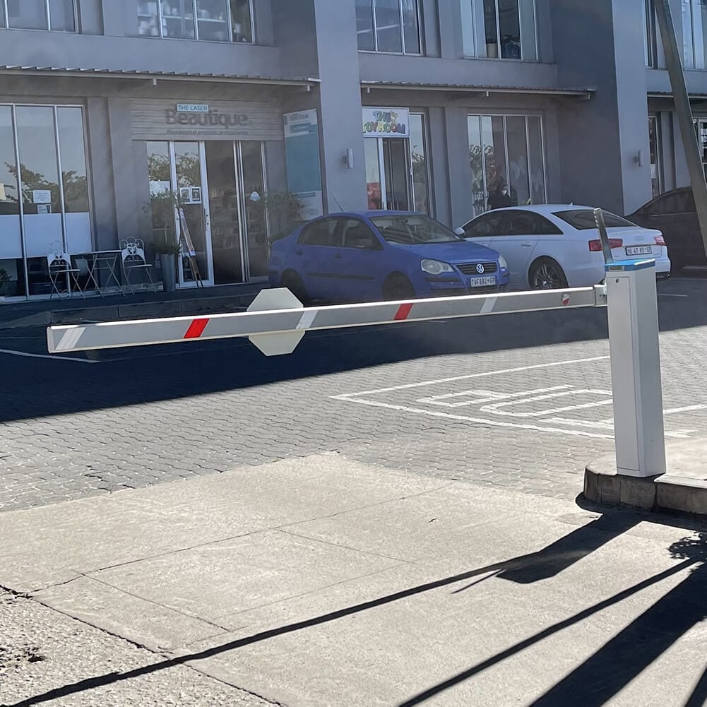 Velocity Manual barrier with a striped boom closing a paved car park in front of an office building.