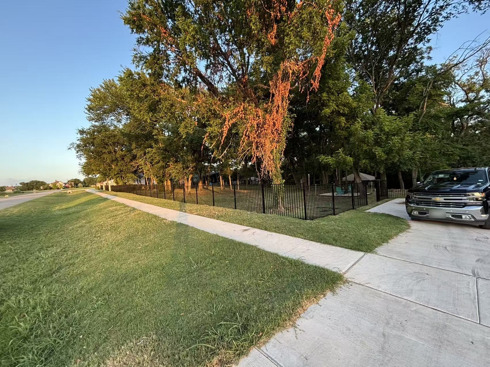 Black flat top ornamental fence around a corner lot beside a driveway, installed view