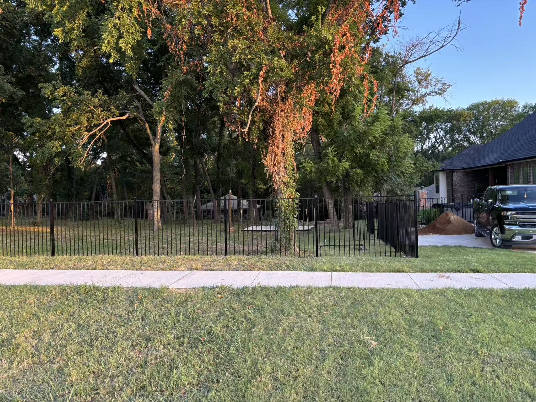 Black flat top ornamental fence in front of a house seen from the sidewalk, installed view