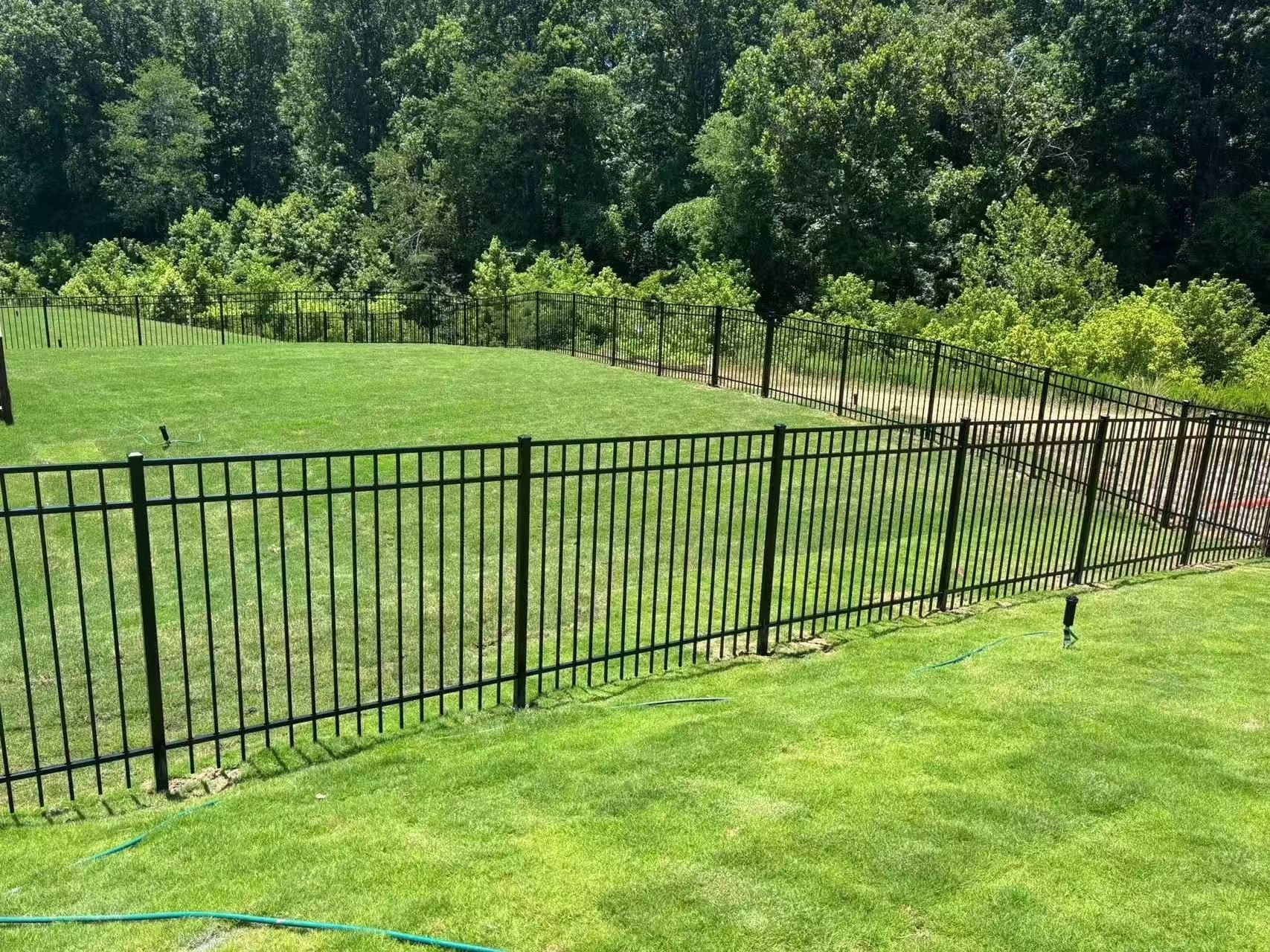 Black flat top ornamental fence following a sloped backyard lawn, installed view