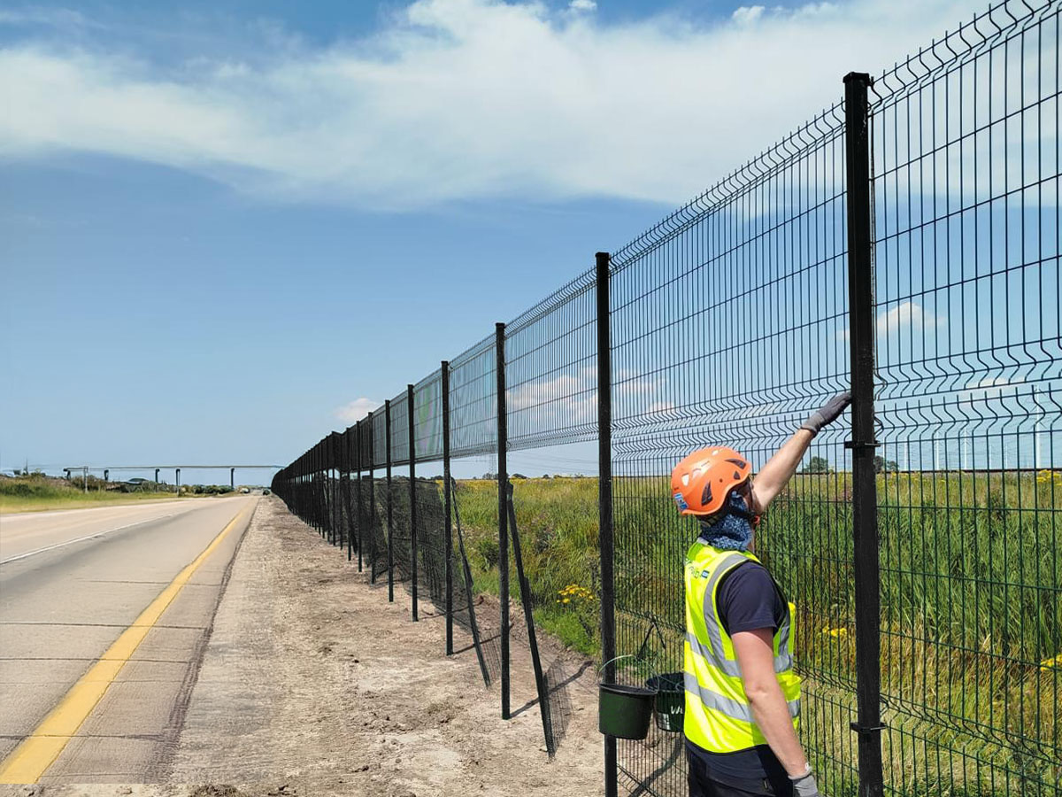 Installer fitting a wire fence along a Texas highway