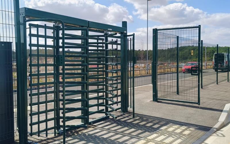 Full-height turnstile with an adjacent pedestrian gate in a mesh fence line