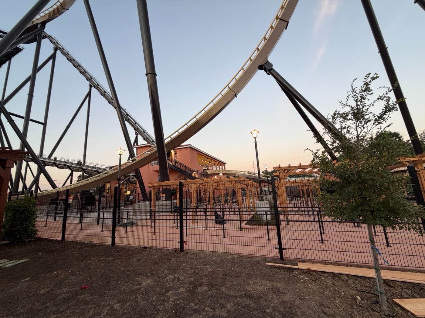 The same Fenceweb fence line at Six Flags Dallas photographed at dusk, with the roller coaster track lit behind it