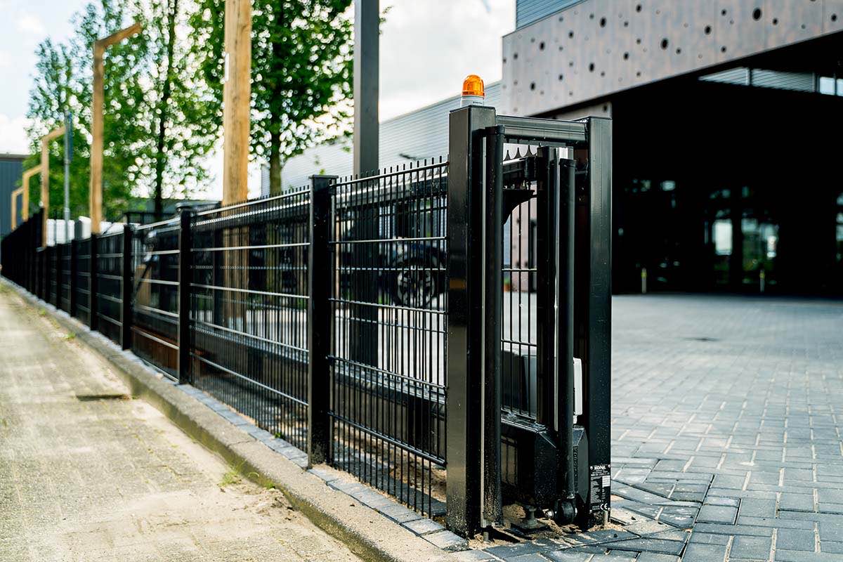 Electric sliding gate with warning light in a fence line at a commercial building